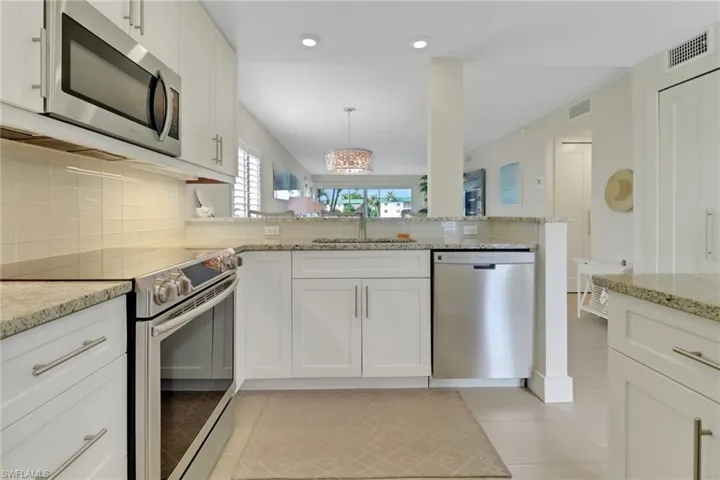 Kitchen with appliances with stainless steel finishes, white cabinets, pendant lighting, light stone counters, and decorative backsplash