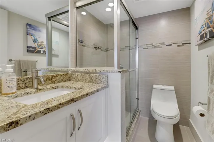 Ensuite bath featuring tile walls, vanity, a stall shower, light tile patterned floors, and recessed lighting