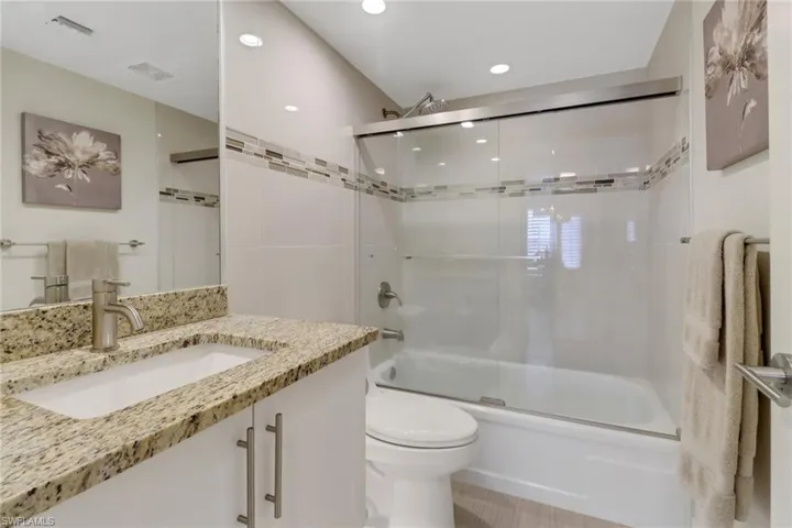 Guest bathroom featuring enclosed tub / shower combo, vanity, and recessed lighting
