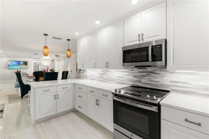 Kitchen featuring stainless steel appliances, white cabinets, open floor plan, decorative light fixtures, and recessed lighting
