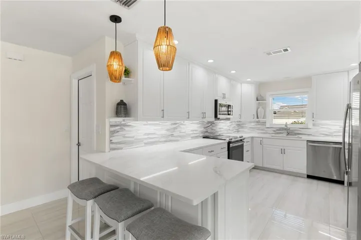 Kitchen with open shelves, a peninsula, white cabinetry, a breakfast bar, and appliances with stainless steel finishes