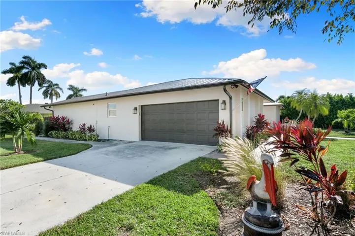 View of front of home with concrete driveway, stucco siding, a garage, a front lawn, and a metal roof