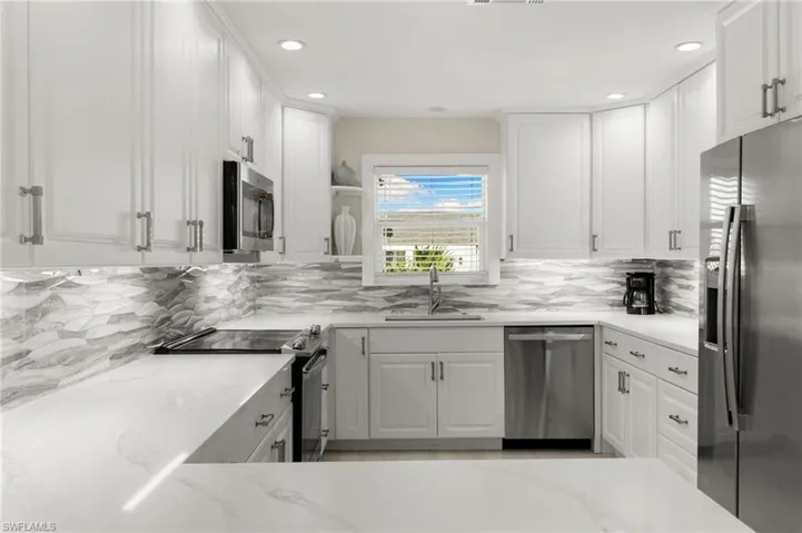 Kitchen with stainless steel appliances, white cabinets, light stone countertops, backsplash, and recessed lighting