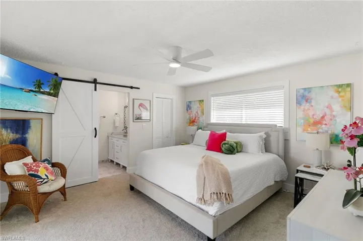 Bedroom with a barn door, connected bathroom, light colored carpet, a ceiling fan, and a textured ceiling
