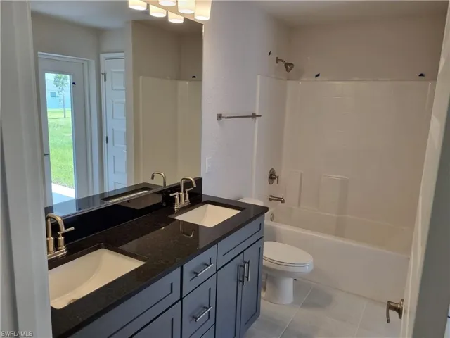 Full bathroom with tile patterned floors, toilet, washtub / shower combination, and vanity