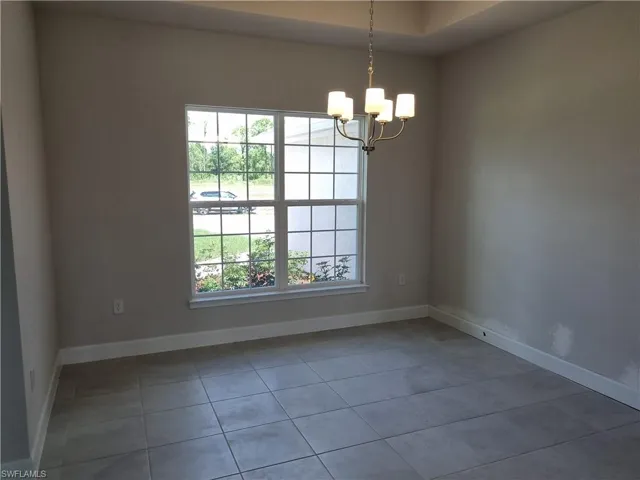 Spare room with tile patterned flooring, a healthy amount of sunlight, and a notable chandelier