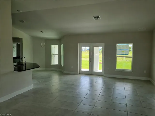 Unfurnished living room with vaulted ceiling, sink, a notable chandelier, and light tile patterned flooring