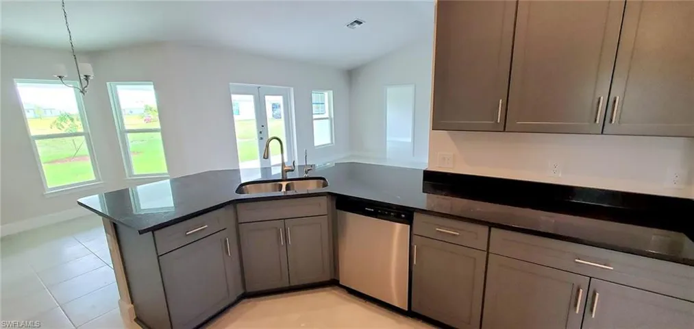 Kitchen featuring dishwasher, vaulted ceiling, sink, kitchen peninsula, and dark stone counters