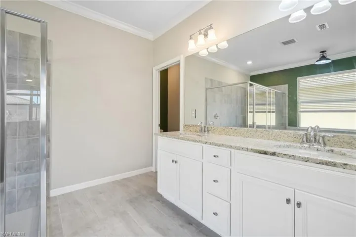 Bathroom featuring crown molding, walk in shower, vanity with extensive cabinet space, and dual sinks