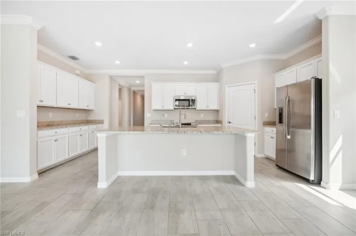 Kitchen featuring light granite countertops, a center island with sink, white cabinets, stainless steel appliances.