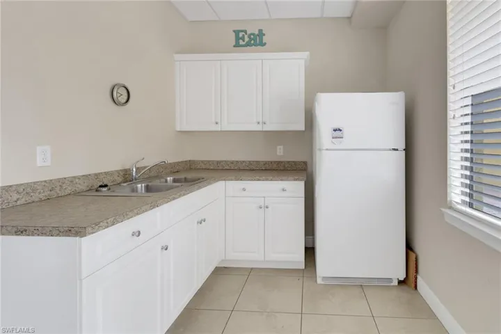 Kitchen with white refrigerator, sink, light tile patterned floors, and white cabinetry