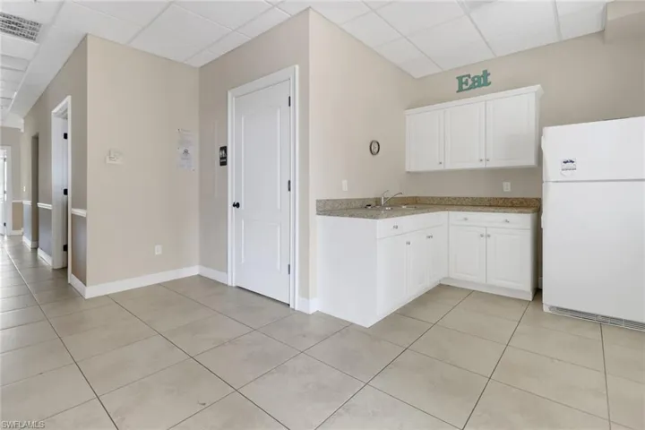 Kitchen featuring white cabinets, white refrigerator, light tile patterned flooring, sink, and a drop ceiling