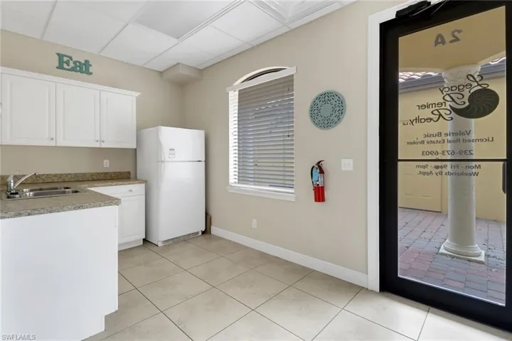 Kitchen with a drop ceiling, sink, white fridge, light tile patterned floors, and white cabinetry
