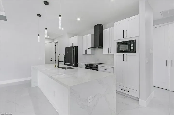 Kitchen featuring wall chimney range hood, a center island with sink, tasteful backsplash, black appliances, and sink