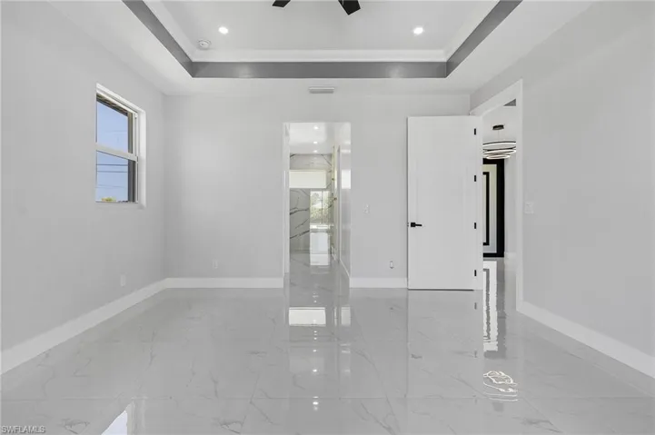 Tiled empty room featuring ceiling fan and a raised ceiling