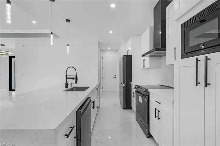 Kitchen featuring decorative light fixtures, black appliances, wall chimney range hood, sink, and white cabinets