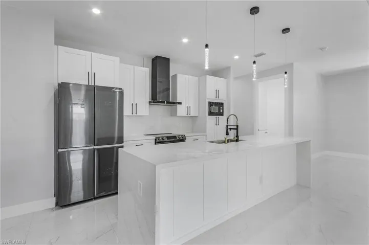 Kitchen with hanging light fixtures, a center island with sink, wall chimney range hood, sink, and appliances with stainless steel finishes