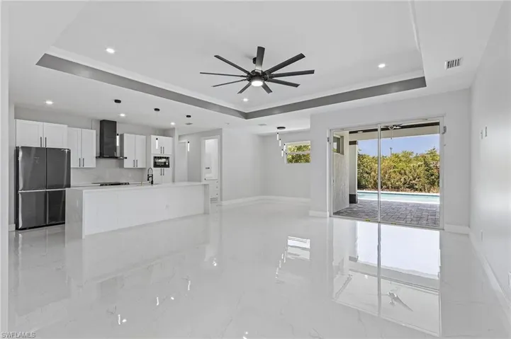 Unfurnished living room featuring sink, light tile flooring, ceiling fan, and a raised ceiling