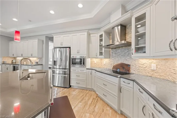 Kitchen featuring decorative backsplash, appliances with stainless steel finishes, ornamental molding, wall chimney range hood, and white cabinetry