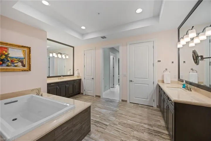Full bath with a tray ceiling, a bath, recessed lighting, and two vanities