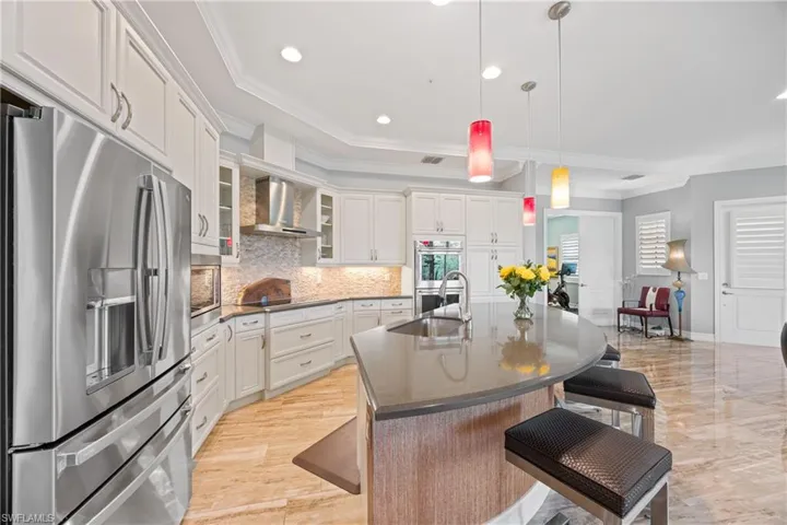 Kitchen featuring appliances with stainless steel finishes, decorative backsplash, ornamental molding, a kitchen bar, and wall chimney exhaust hood