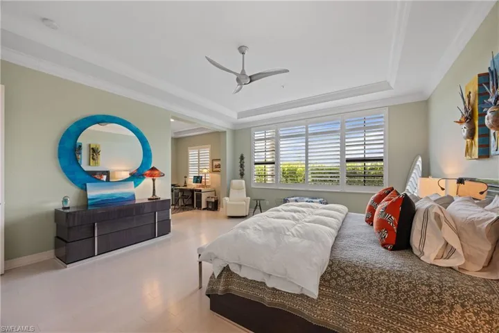 Bedroom with crown molding, custom Maple wood finished floors, a tray ceiling, and a ceiling fan