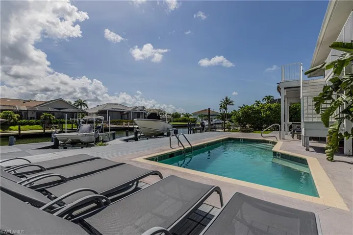 Outdoor pool with boat lift, a boat dock, a patio, and a water view