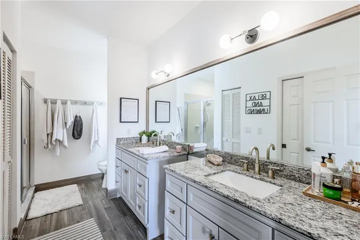 Bathroom featuring a shower stall, two vanities, and wood finished floors