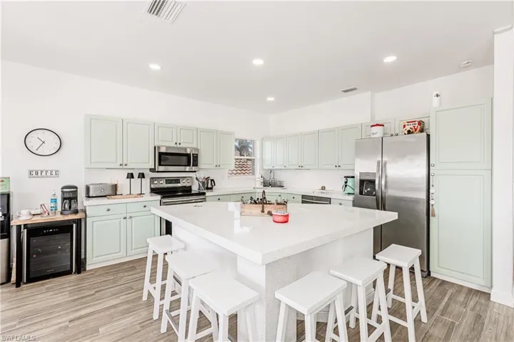Kitchen featuring appliances with stainless steel finishes, wine cooler, a breakfast bar, light countertops, and recessed lighting