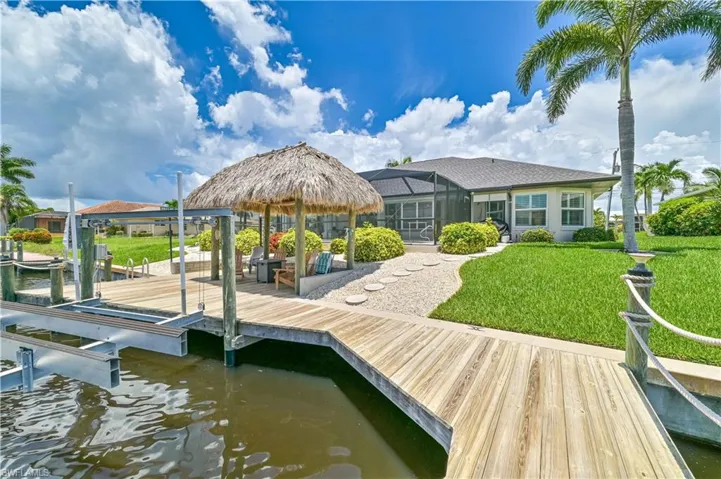 Dock area with glass enclosure, a water view, and a lawn
