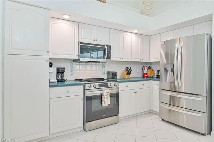 Kitchen with stainless steel appliances, white cabinets, backsplash, light tile patterned floors, and ornamental molding