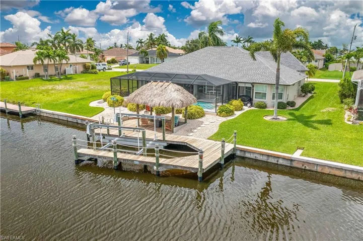 View of dock featuring a water view, a lanai, and a lawn