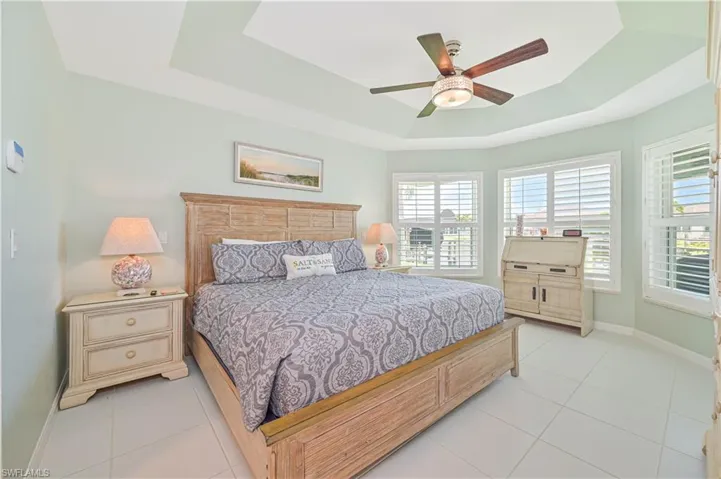 Bedroom with a raised ceiling, light tile patterned floors, and ceiling fan