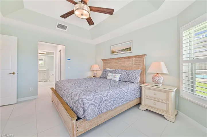 Tiled bedroom with ensuite bath, ceiling fan, and a tray ceiling