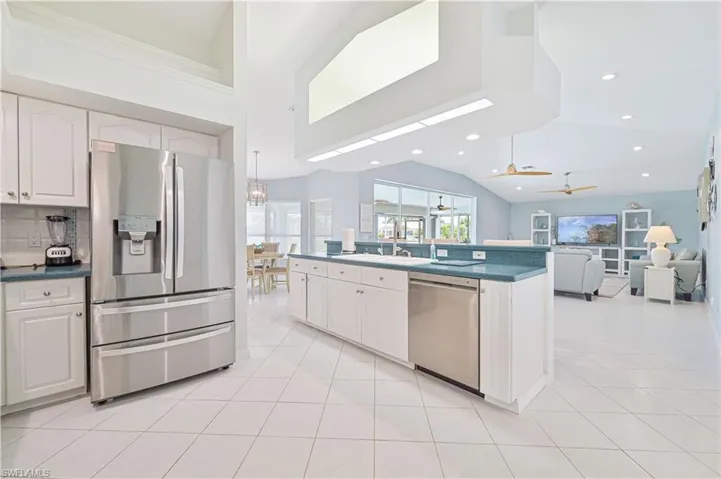 Kitchen with appliances with stainless steel finishes, sink, ceiling fan with notable chandelier, high vaulted ceiling, and white cabinetry