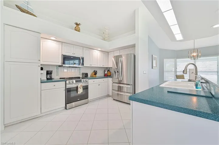 Kitchen featuring light tile patterned flooring, tasteful backsplash, hanging light fixtures, white cabinets, and appliances with stainless steel finishes