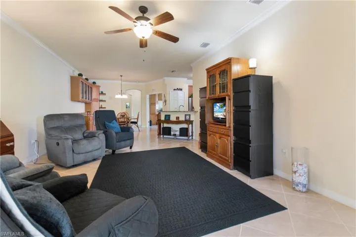 Tiled living room with ceiling fan with notable chandelier and crown molding