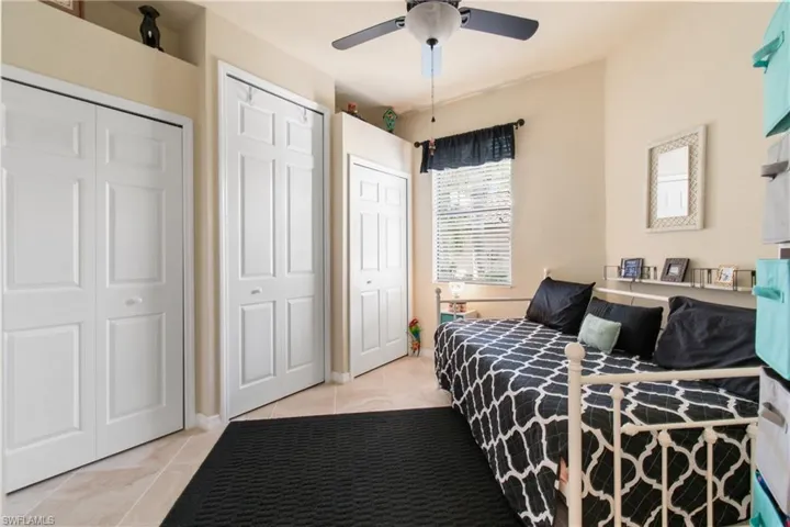 Bedroom with ceiling fan, light tile patterned flooring, and multiple closets