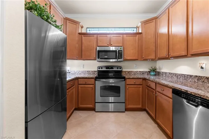 Kitchen with light tile patterned flooring, stainless steel appliances, ornamental molding, and dark stone countertops