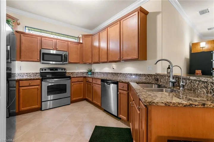 Kitchen with kitchen peninsula, dark stone counters, ornamental molding, stainless steel appliances, and sink