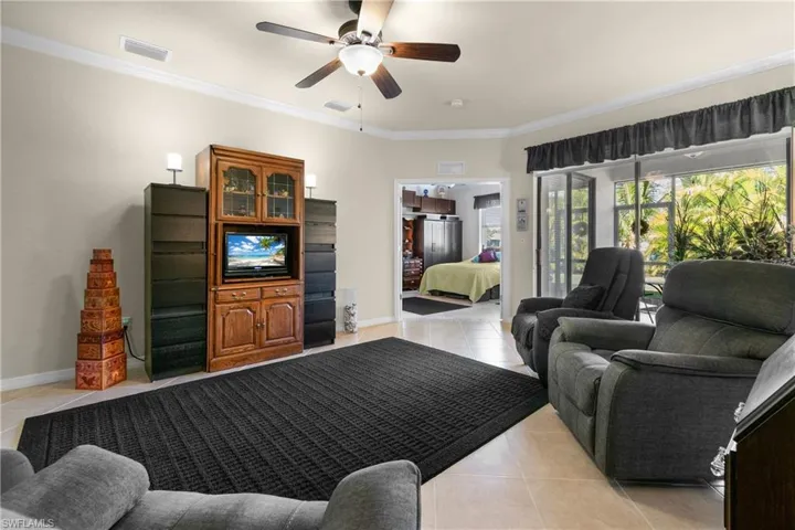 Living room with ceiling fan, light tile patterned floors, and crown molding
