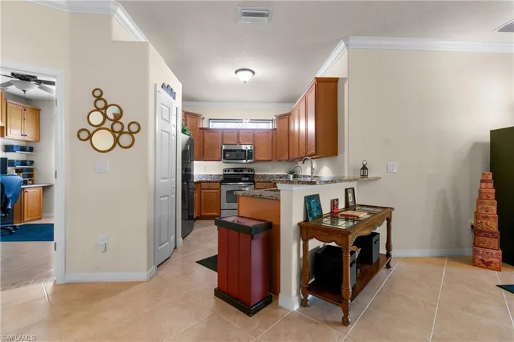 Kitchen featuring kitchen peninsula, light tile patterned floors, stainless steel appliances, and ornamental molding