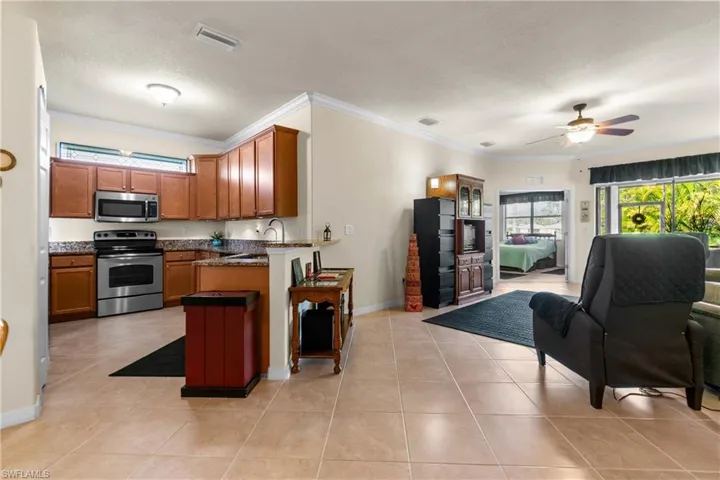 Kitchen with a textured ceiling, stainless steel appliances, ceiling fan, crown molding, and light tile patterned flooring