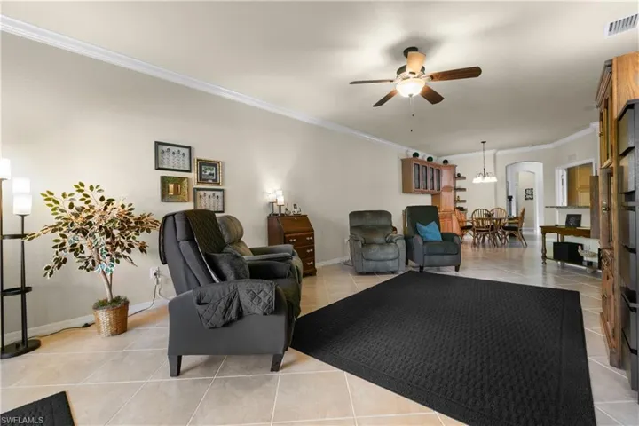 Tiled living room featuring ceiling fan with notable chandelier and ornamental molding