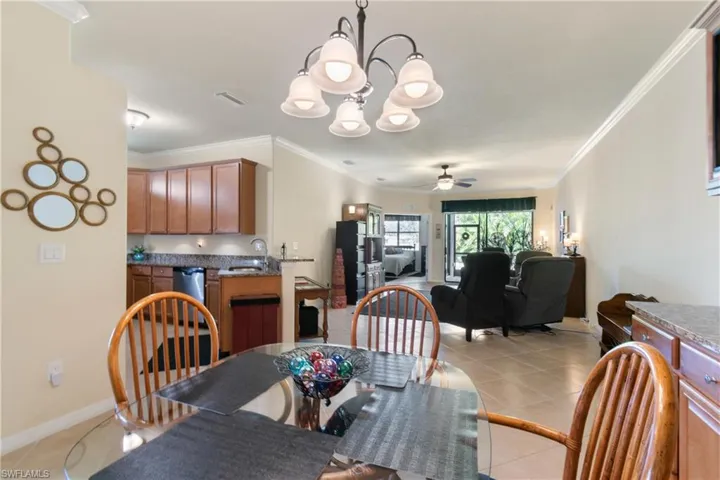 Dining space with crown molding, sink, light tile patterned flooring, and ceiling fan with notable chandelier