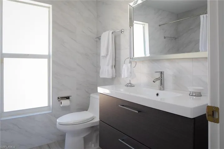 Bathroom featuring vanity, tile walls, and toilet