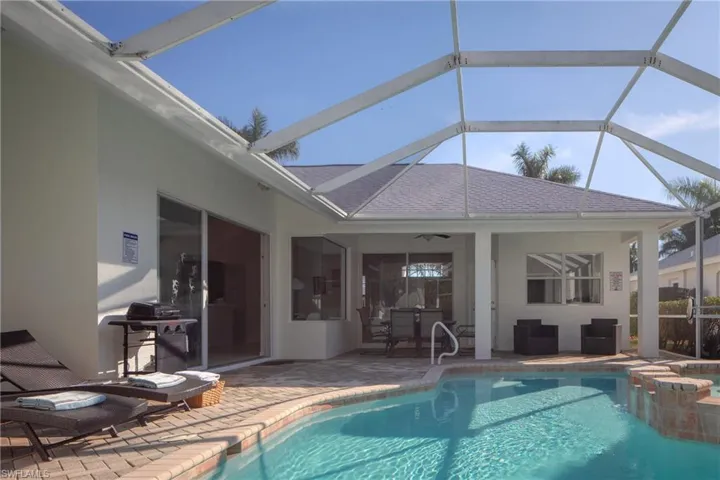 View of pool with grilling area, a patio area, ceiling fan, and glass enclosure