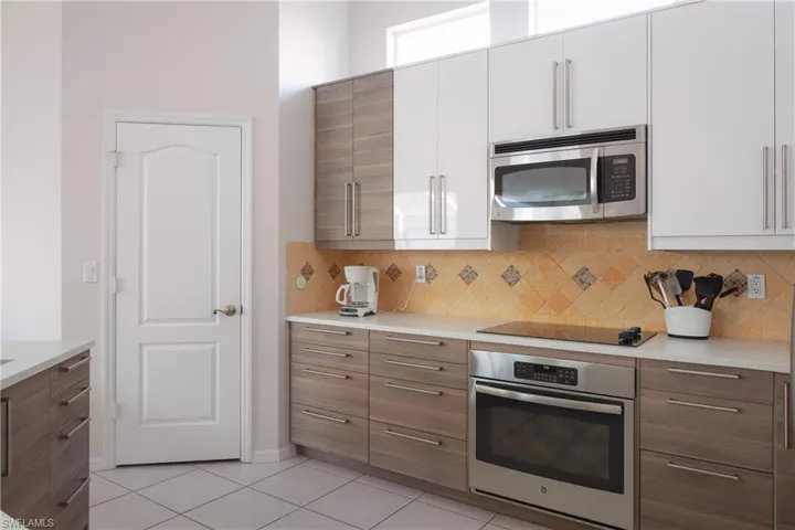 Kitchen featuring backsplash, stainless steel appliances, white cabinets, and light tile patterned flooring
