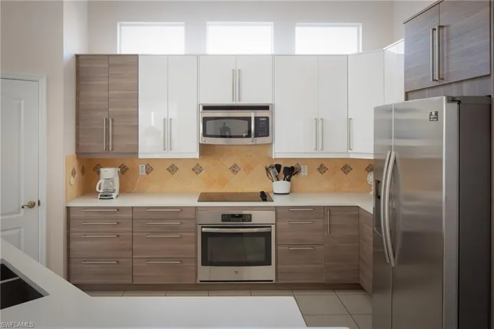 Kitchen featuring appliances with stainless steel finishes, light tile patterned floors, white cabinets, and decorative backsplash