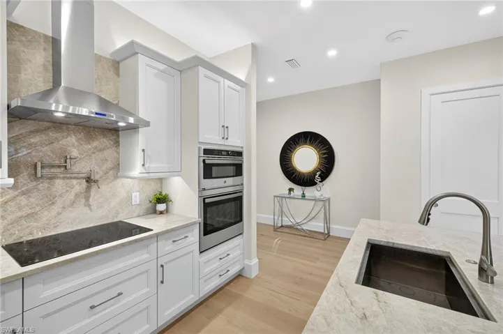 Kitchen featuring light stone countertops, wall chimney range hood, black electric cooktop, tasteful backsplash, and light wood-type flooring